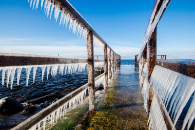 Güneşli bir günde, karla kaplı eski, paslı iskele. Buz parçaları yakın plan. Baltık Denizi, Letonya