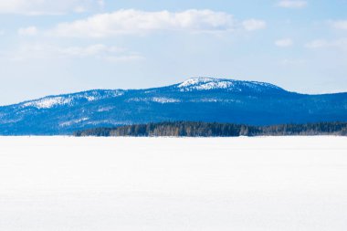 Donmuş gölün panoramik manzarası. Arka planda karla kaplı dağlar ve kozalaklı ormanlar var. Açık mavi gökyüzü. Kola Yarımadası, Murmansk bölgesi, Kutup Dairesi, Karelia, Rusya