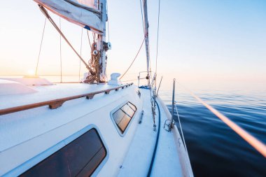 Sakin su. Günbatımında beyaz yelkenli tekneyle denize açılacak. Güverteden pruvaya, direğe ve yelkenlere bir manzara. Baltık Denizi, Letonya