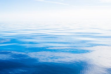 Deniz suyu dokusu. Açık mavi gökyüzü, beyaz bulutlar ve uçak izleri. Sudaki yansımalar. Baltık Denizi, Estonya