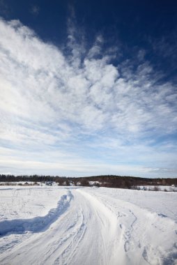 Karla kaplı tarlalarda traktör izleri olan toprak yol manzarası. Dramatik mavi gökyüzü. Arka planda orman var. Kuito Gölü, Karelia Kuzey, Laponya