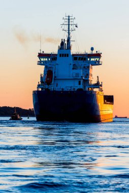 Gün batımında büyük bir kargo gemisi, yakın plan. Arka planda deniz feneri var. Riga, Letonya