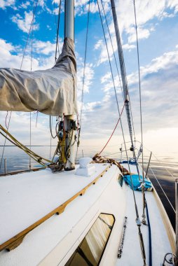 Gün batımında durgun suda yüzen beyaz bir yat. Güverteden pruvaya, direğe ve yelkenlere bir manzara. Şaşırtıcı bulut manzarası. Doğal ayna. Spor ve eğlence teması. Baltık Denizi, Letonya
