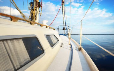 Gün batımında durgun suda yüzen beyaz bir yat. Güverteden pruvaya, direğe ve yelkenlere bir manzara. Şaşırtıcı bulut manzarası. Doğal ayna. Spor ve eğlence teması. Baltık Denizi, Letonya