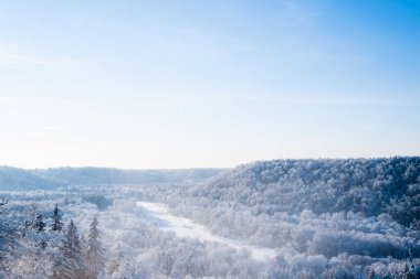 Sabah sisli bir kar fırtınasından sonra nehrin ve karla kaplı ormanın havadan görünüşü. Açık mavi gökyüzü. Kış Harikalar Diyarı. Gauja Ulusal Parkı, Sigulda, Letonya