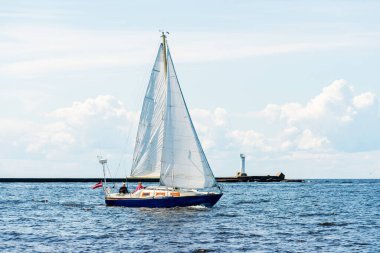 Açık bir günde mavi yelkenli yelkenli yelkenli. Arka planda deniz feneri var. Riga Körfezi, Baltık Denizi, Letonya