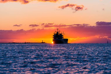 Günbatımında Baltık Denizi 'nde kargo gemisi. Arka planda deniz feneri var. Şaşırtıcı bulut manzarası. Letonya