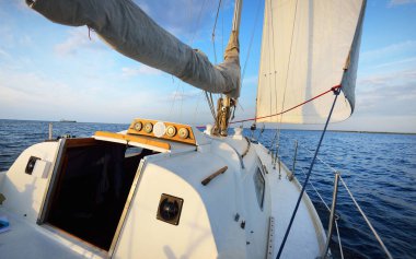 Gün batımında durgun suda yüzen beyaz bir yat. Güverteden pruvaya, direğe ve yelkenlere bir manzara. Şaşırtıcı bulut manzarası. Doğal ayna. Spor ve eğlence teması. Baltık Denizi, Letonya