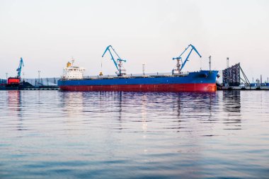 Kargo gemisi gün batımında Letonya, Riga limanında. Arka planda port vinçleri