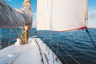 Gün batımında durgun suda yüzen beyaz bir yat. Güverteden pruvaya, direğe ve yelkenlere bir manzara. Şaşırtıcı bulut manzarası. Doğal ayna. Spor ve eğlence teması. Baltık Denizi, Letonya
