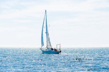 Akdeniz 'de güneşli bir günde, İspanya' da beyaz yelkenli dolu bir yat. Beyaz bulutlu mavi gökyüzü, suda yansımalar.;
