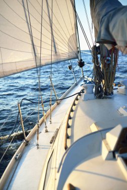 Güneşli bir günde beyaz bir yat denize açılıyor. Güverteden pruva ve yelkenlere kadar yakın çekim. Dalgalar ve su sıçramaları. Britanya, Fransa