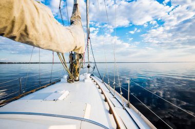 Gün batımında durgun suda yüzen beyaz bir yat. Güverteden pruvaya, direğe ve yelkenlere bir manzara. Şaşırtıcı bulut manzarası. Doğal ayna. Spor ve eğlence teması. Baltık Denizi, Letonya