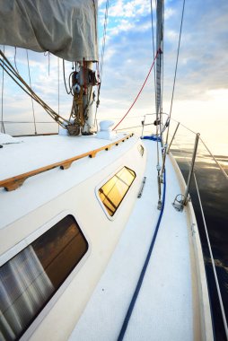 Gün batımında durgun suda yüzen beyaz bir yat. Güverteden pruvaya, direğe ve yelkenlere bir manzara. Şaşırtıcı bulut manzarası. Doğal ayna. Spor ve eğlence teması. Baltık Denizi, Letonya