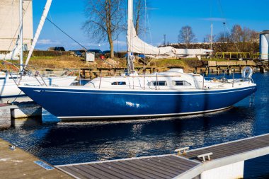 Kışın kışı geçirdikten sonra bir rıhtıma demirlenmiş mavi şalopa. Açık mavi gökyüzü. Riga Limanı, Letonya