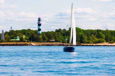 Açık bir günde mavi yelkenli yelkenli yelkenli. Arka planda deniz feneri ve orman var. Riga Körfezi, Baltık Denizi, Letonya