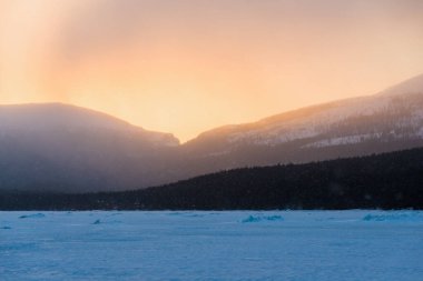 Gün batımında kar fırtınasından sonra Kandalaksha koyunda. Altın akşam bulutları. Arka planda Kola Yarımadası 'nın dağları ve kozalaklı ormanları var. Beyaz deniz, Kutup dairesi, Karelia, Rusya