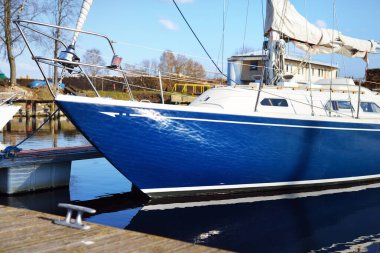 Kışın kışı geçirdikten sonra bir rıhtıma demirlenmiş mavi şalopa. Açık mavi gökyüzü. Arka planda yakacak odun var. Riga Limanı, Letonya