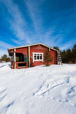 Karla kaplı tepenin üzerindeki eski kırmızı ahşap ev, arka planda çam ormanı. İnsanlar koronavirüs (COVID-19) salgını nedeniyle evde kalıyorlar. Karelia North. Laponya. Kuito Gölü
