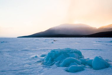 Gün batımında kar fırtınasından sonra Kandalaksha koyunda. Altın akşam bulutları. Arka planda Kola Yarımadası 'nın dağları ve kozalaklı ormanları var. Beyaz deniz, Kutup dairesi, Karelia, Rusya