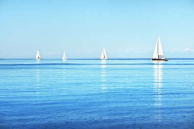 Açık ve güneşli bir günde Akdeniz 'de yelkenli dolu yatlar. Beyaz bulutlu mavi gökyüzü, suda yansımalar.