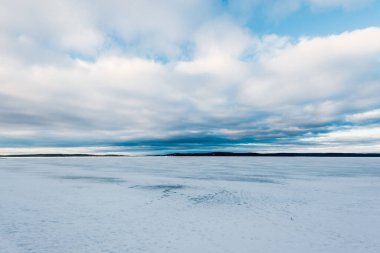 Kış manzarası. Gün batımında donmuş karla kaplı göl manzarası. Arka planda orman var. Renkli akşam bulutları. Onega Gölü, Karelia, Rusya