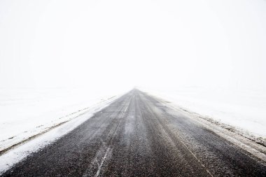 Bulutlu bir kış gününde, Letonya 'nın karla kaplı tarlalarında boş bir köy yolu.