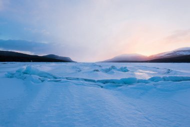 Gün batımında Kandalaksha Körfezi 'nin buz basıncı sırtı. Renkli akşam bulutları. Arka planda Kola Yarımadası 'nın dağları ve kozalaklı ormanları var. Beyaz deniz, Kutup dairesi, Karelia, Rusya