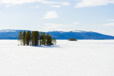 Donmuş gölün panoramik manzarası. Arka planda karla kaplı dağlar ve kozalaklı ormanlar var. Açık mavi gökyüzü. Kola Yarımadası, Murmansk bölgesi, Kutup Dairesi, Karelia, Rusya