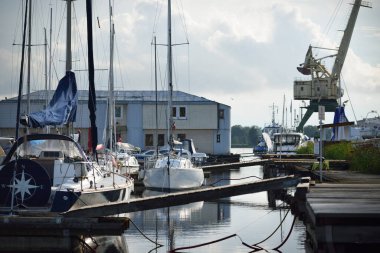 Açık bir yaz gününde rıhtıma demirlenmiş yat ve tekneler, yakın çekim. Sudaki yansımalar. Riga Limanı, Letonya