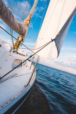 Mavi yat gün batımında Norveç 'te nehirde yüzüyor. Güverteden pruvaya ve yelkenlere bir manzara. Açık mavi gökyüzü. Spor ve eğlence teması