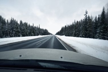 Bir kar fırtınasında kozalaklı ormanda boş asfalt yolu manzarası. İnsanlar Coronavirus (COVID-19) salgını yüzünden evlerine dönüyorlar. Onega Gölü, Karelia, Rusya