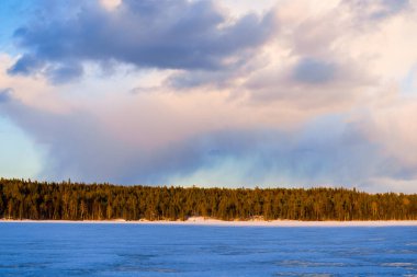Karla kaplı donmuş Kuito gölünün üzerinde dramatik bir günbatımı gökyüzü, arka planda kozalaklı bir orman. Kış kır manzarası. Renkli bulutlar. Karelya Kuzey, Laponya