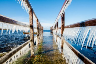 Güneşli bir günde, karla kaplı eski, paslı iskele. Buz parçaları yakın plan. Baltık Denizi, Letonya