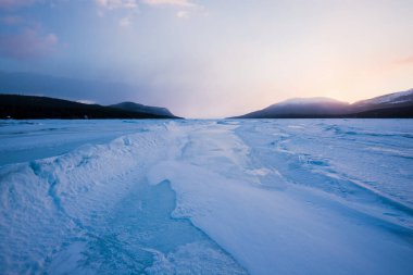 Gün batımında Kandalaksha Körfezi 'nin buz basıncı sırtı. Renkli akşam bulutları. Arka planda Kola Yarımadası 'nın dağları ve kozalaklı ormanları var. Beyaz deniz, Kutup dairesi, Karelia, Rusya