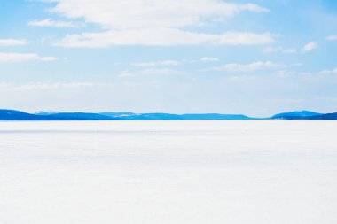 Donmuş gölün panoramik manzarası. Arka planda karla kaplı dağlar ve kozalaklı ormanlar var. Açık mavi gökyüzü. Kola Yarımadası, Murmansk bölgesi, Kutup Dairesi, Karelia, Rusya