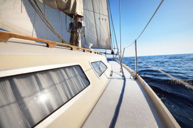 Güneşli bir yaz gününde beyaz bir yat denize açılıyor. Güverteden pruva ve yelkenlere kadar yakın çekim. Dalgalar ve su sıçramaları. Açık mavi gökyüzü. Baltık Denizi, İsveç. Ulaşım, spor, eğlence aktivitesi