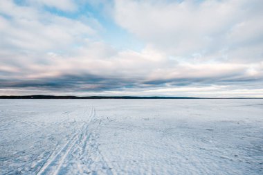 Kış manzarası. Gün batımında donmuş karla kaplı göl manzarası. Arka planda orman var. Renkli akşam bulutları. Onega Gölü, Karelia, Rusya