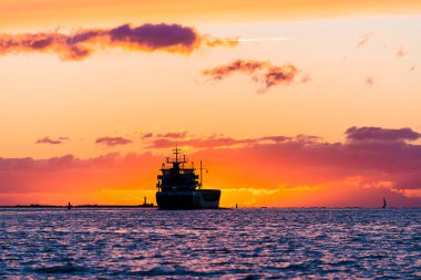 Günbatımında Baltık Denizi 'nde kargo gemisi. Arka planda deniz feneri var. Şaşırtıcı bulut manzarası. Letonya