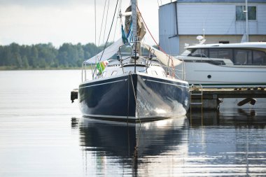 Açık bir yaz gününde açık bir rıhtıma demirlenmiş mavi şalopeli yat, yakın çekim. Arka planda tekneler var. Riga Limanı, Letonya