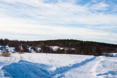 Karla kaplı tarlalarda traktör izleri olan toprak yol manzarası. Dramatik mavi gökyüzü. Arka planda orman var. Kuito Gölü, Karelia Kuzey, Laponya