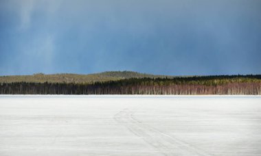 Karla kaplı donmuş Kuito gölünün üzerindeki dramatik mavi gökyüzü, arka planda kozalaklı orman. Kış kır manzarası. Fırtına bulutları. Karelya Kuzey, Laponya