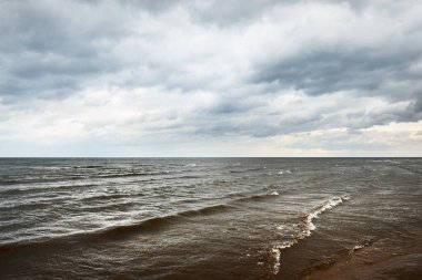 Baharda Baltık Denizi 'nin kumlu kıyılarında fırtına bulutları, dramatik gökyüzü, dalgalar ve su sıçramaları. Koyu deniz manzarası. - Letonya. Hava, iklim değişikliği, ekoloji, çevre, doğa