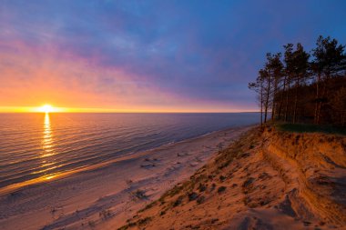 Letonya 'nın Baltık kıyıları üzerinde çarpıcı günbatımı bulutları. Kum tepeleri ve çam ağaçları yakın plan. Altın akşam güneşi. Yaz manzarası