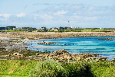Plouguerneau, Brittany, Fransa 'daki Rocky okyanus kıyısı. Arka planda evler ve deniz feneri var.