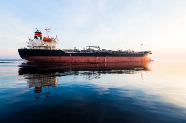 Gün batımında büyük bir kargo gemisi. Renkli akşam bulutları ve parlak güneş ışığı. Baltık Denizi, Letonya