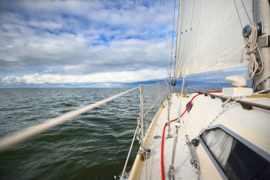 Beyaz yat gün batımında denize açılacak. Güverteden pruvaya bir manzara. Parlayan renkli bulutları olan dramatik gökyüzü, suda simetri yansımaları, doğal ayna. Destansı bulut manzarası. Hanko Yarımadası, Finlandiya