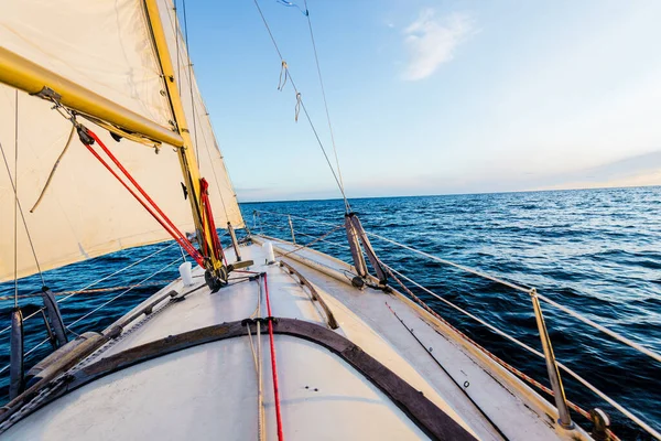 Sloop rigged yacht sailing on a clear day. A view from the deck to the bow and sails. Waves and water splashes. Baltic sea, Latvia