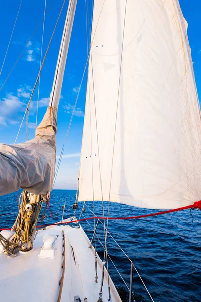 White yacht sailing in a still water at sunset. A view from the deck to the bow, mast and sails. Stunning cloudscape. Natural mirror. Sport and recreation theme. Baltic sea, Latvia