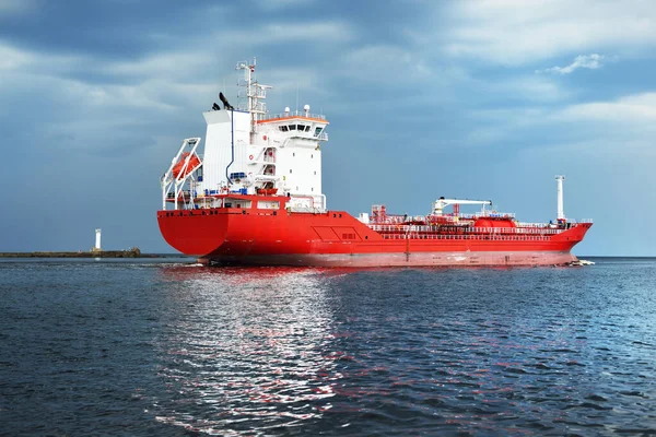 オープンバルト海でクレーン付きの大きな赤い貨物船 暗い嵐の雲 背景に灯台 ラトビア — ストック写真